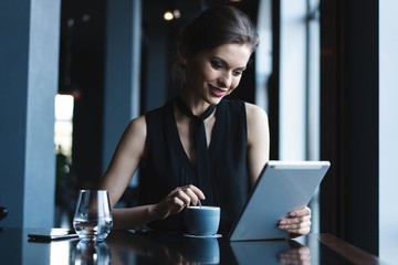 Young attractive woman sitting in coffee shop during free time and working on tablet computer. Happy female having rest in cafe. Lifestyle.