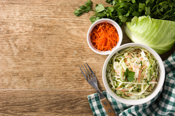 Coleslaw salad in white bowl and ingredients on wooden table. Top view