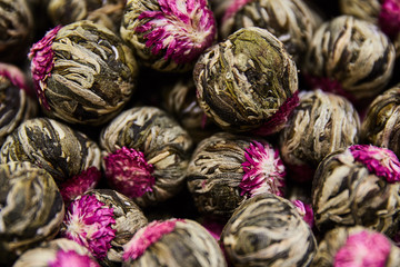 Fototapeta na wymiar Blooming jasmine tea balls dry with pink flower. Close up, horizontal. Asian tea delight concept. 