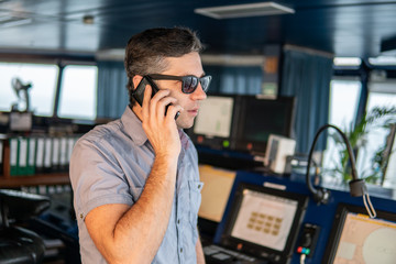 Marine Deck Officer or seaman on navigation bridge of vessel or ship . He is speaking on the mobile...
