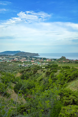 Fototapeta na wymiar Sudak, Crimean Republic, Russia - May 30, 2017: View of the district of Sudak, residential buildings. Terrain in the mountains, vineyards, the sea on the horizon. View of Alchak mountain.