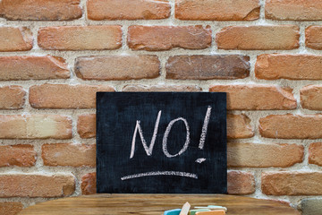 Chalk board with the word NO! drown by hand and chalks on wooden table on brick wall background.