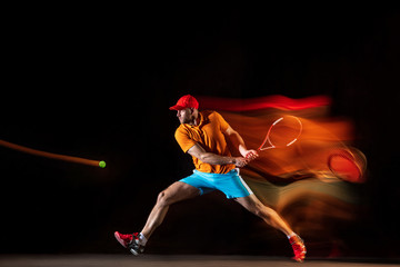 One caucasian man playing tennis isolated on black background in mixed light. Studio shot of fit...