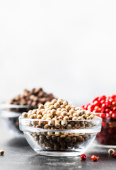 Black, white and pink rose peppers in bowls, assorted spices on gray kitchen table, selective focus