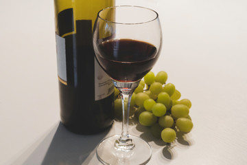Rotwein mit einem gefüllten Weinglas und grünen Weintrauben