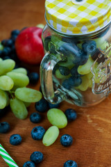 seasonal fruits. red nectarines, green grapes on light wooden background with glass transparent mug filled