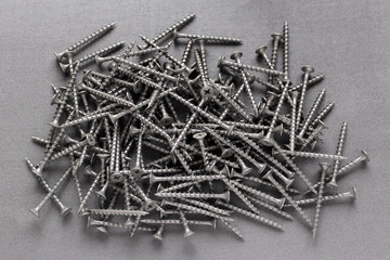Pile of nails on grey background. Screws. Wood screws pile on aged wooden surface. 