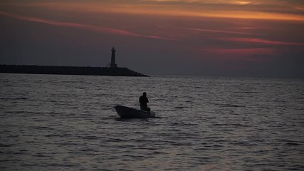 the silhouette of the boat is floating at sunset on the sea by the lighthouse