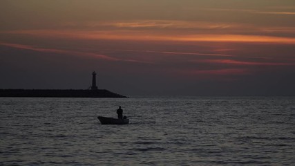 the silhouette of the boat is floating at sunset on the sea by the lighthouse