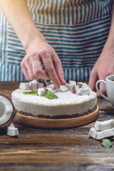 Obraz na płótnie Canvas Confectioner decorates coconut raw cake with white pulp and mint. Healthy vegan dessert. Gluten and sugar free food