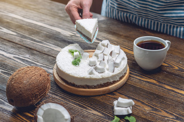 Confectioner holding a piece of coconut raw cake with white pulp. Healthy vegan dessert. Gluten and sugar free food
