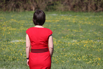 Vacation and summer leisure, woman in red dress on a green meadow with flowers, rear view. Harmony with nature, concept of ecology, dreaming, female fashion