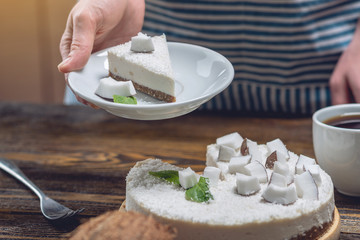 Confectioner holding a piece of coconut raw cake with white pulp and mint. Healthy vegan dessert. Gluten and sugar free