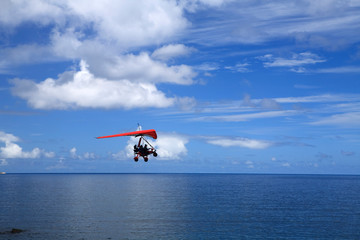 Fototapeta na wymiar An extreme sport enthusiast flies a microlight across the ocean with blue sky and fluffy clouds in the background