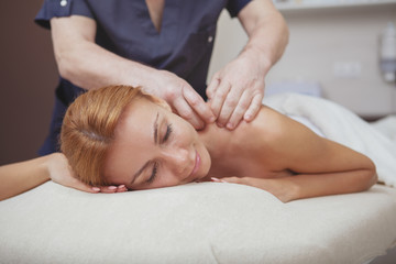 Cropped shot of a professional masseur working at his spa center, massaging back of a gorgeous woman. Beautiful female smiling with eyes closed, getting back massage