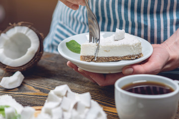 Confectioner holding a piece of coconut raw cake with white pulp and mint. Healthy vegan dessert. Gluten and sugar free