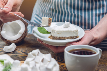 Piece of coconut raw cake with white pulp and mint on a wooden background. Vegan dessert. Gluten and sugar free food