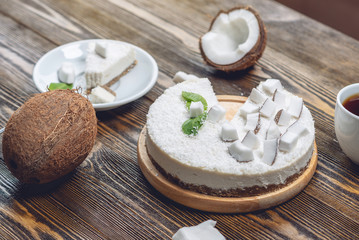Obraz na płótnie Canvas Raw coconut cake decorated with white coconut pulp and mint on a wooden background. Healthy vegan dessert.
