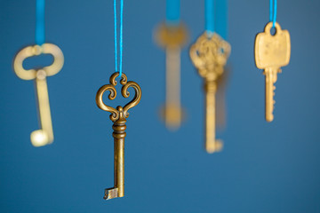 Many old keys of yellow gold color are hanging on thread on a blue background. The concept of the selection of access or password to the secret data