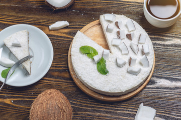 Raw coconut cake decorated with white coconut pulp and mint on a wooden background. Healthy vegan dessert.