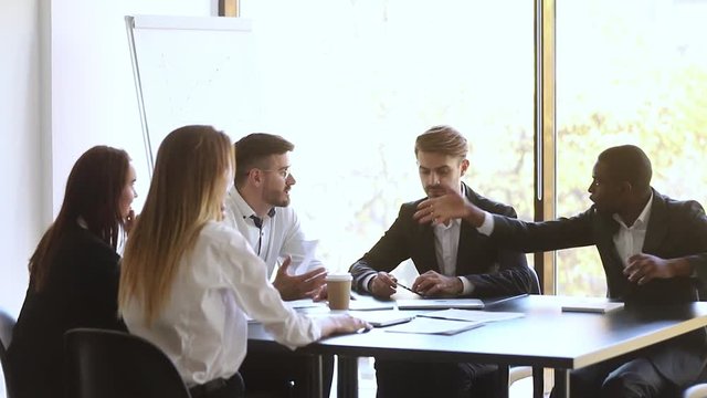 Mad african caucasian colleagues disputing throwing papers fighting at work