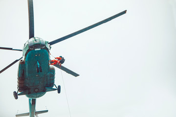 Rescue helicopter and rescuer on the rope - life-saving flying vehicle on the rainy sky background.