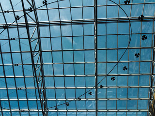 Metal construction under the glass roof of the shopping center, through which the blue sky is visible