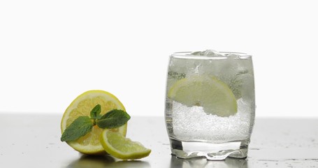 Glass with a cold drink with leaves of mint, lime, lemon and ice cubes