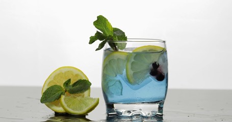 Glass with cold blue drink with leaves of mint, lime, lemon, black currants