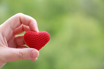Red heart in female hands on green nature background, free copy space for text. Woman with knitted...