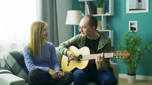 the guy plays his girlfriend on the guitar in the living room
