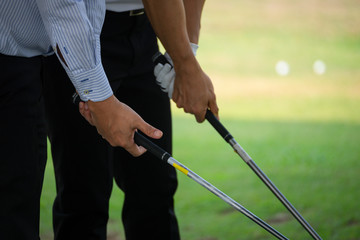 The hands of two golfers who are holding golf clubs.
