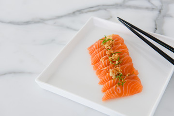 Sliced salmon sashimi on white plate with chopsticks and white background