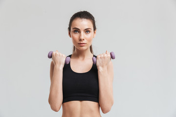 Fototapeta na wymiar Young sport fitness woman make exercises with dumbbells isolated over grey wall background.