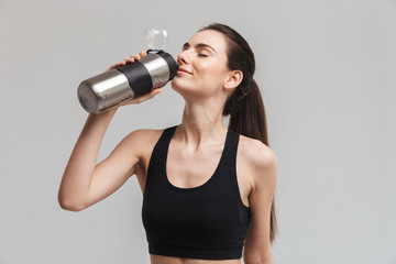 Beautiful young sport fitness woman drinking water isolated over grey wall background.