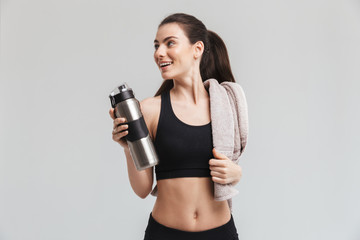 Beautiful young sport fitness woman drinking water isolated over grey wall background.