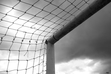 cropped shot of the postage stamp of a Soccer Goal net and post and crossbar joint with grey sky. ...