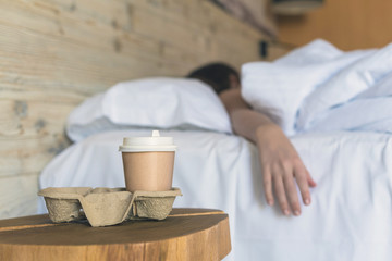 .A paper cup of coffee standing on the table in the bedroom in the early morning as a surprise for a sleeping