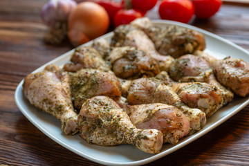 Raw chicken legs with herbs and spices on white dish. Top view. Food ingredient.