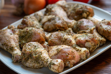 Raw chicken legs with herbs and spices on white dish. Top view. Food ingredient.