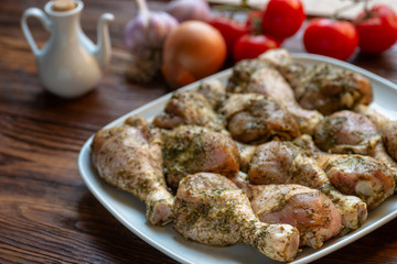 Raw chicken legs with herbs and spices on white dish. Top view. Food ingredient.