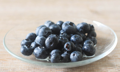 Blueberry in glass plate on wooden background.