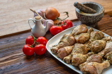 Raw chicken legs with herbs and spices on white dish.