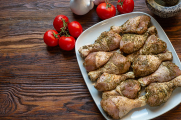 Raw chicken legs with herbs and spices on white dish.