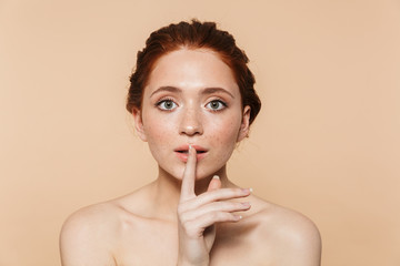 Young redhead woman posing isolated over beige wall background showing silence gesture.