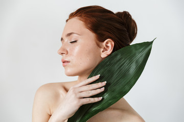 Young redhead woman posing isolated over white wall background with leaf green flowers.