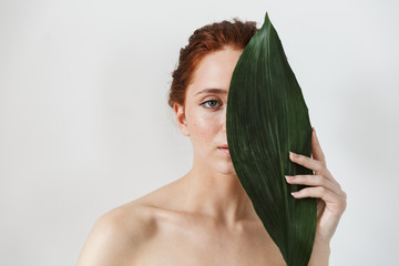 Young redhead woman posing isolated over white wall background with leaf green flowers.