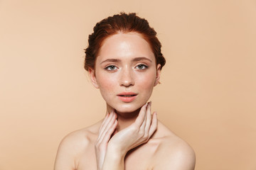 Young redhead woman posing isolated over beige wall background.