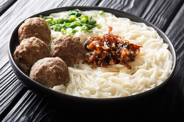 Spicy Indonesian bakso meatballs with noodles, caramelized onions, greens and broth close-up on a plate. horizontal