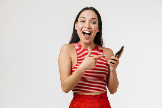 Image of exited asian woman wearing casual clothes holding cellphone and pointing finger at copyspace